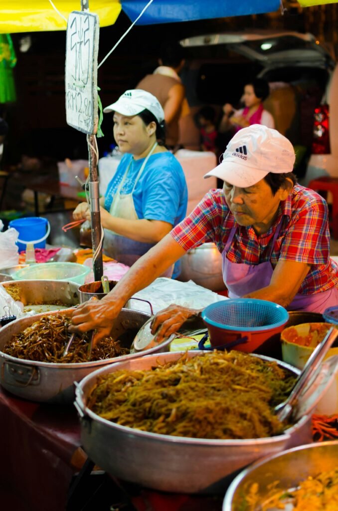 Street food vendors in Malaysia serve a variety of noodle dishes at a vibrant night market.